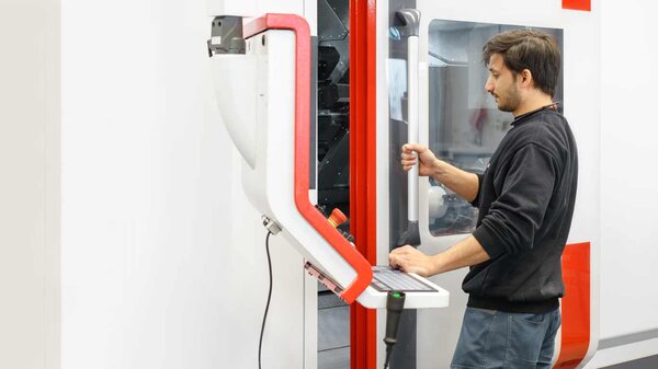 telle-Mitarbeiter öffnet die Tür der CNC-Universaldrehmaschine.